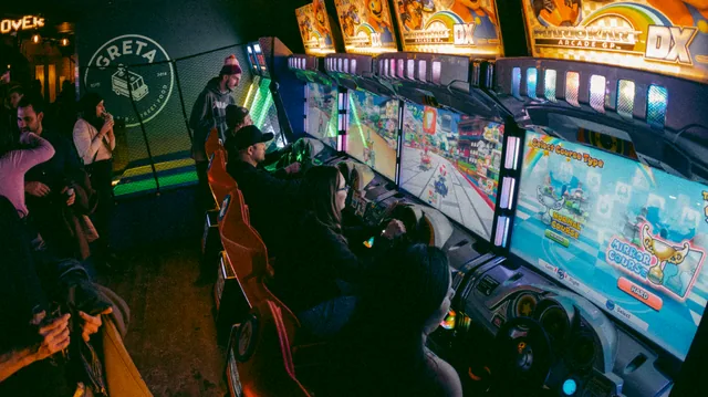Row of Mario Kart arcade machines with players seated, inside the Greta venue in Calgary.