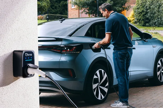Man plugging a grey electric car into an Ohme home charger mounted on a white wall.