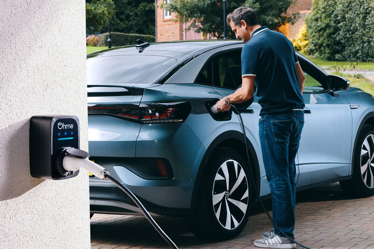 Man plugging a grey electric car into an Ohme home charger mounted on a white wall.