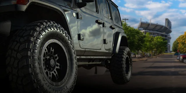 Fortune Tires hero image of a Fortune tire on a grey Jeep in front of a stadium.