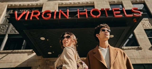 Promotional image associated with the Virgin Radio Rate My Day with Virgin Red competition, showing two people outside Virgin Hotels.